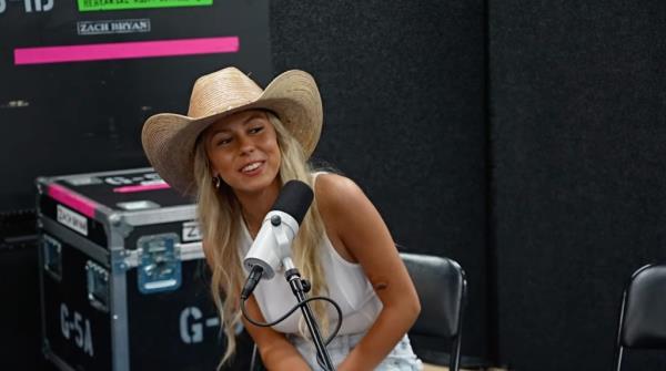 Hailey Welch, also known as 'Hawk Tuah Girl', sitting in front of a microphone and wearing a cowboy hat during her first interview after going viral.