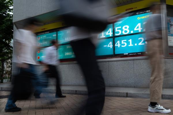 Pedestrians in Tokyo walking past mo<em></em>nitors displaying the significantly declined Nikkei 225 Stock Average outside a securities firm