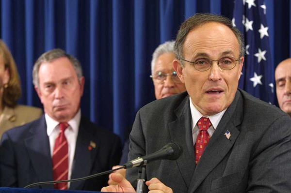 Rudy Giuliani and Michael Bloomberg. A man in a suit speaking into a microphone.