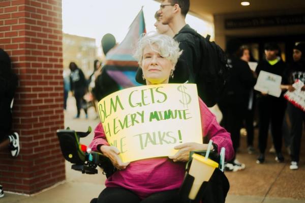 A woman holds a sign as she and others gathered on campus to protest the appearance of Kyle Rittenhouse.