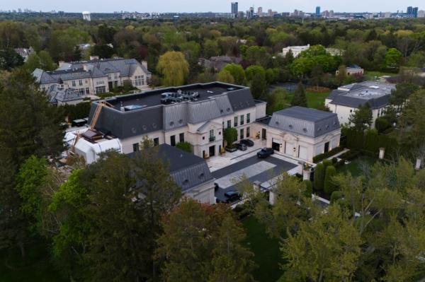 A cream colored mansion with a dark gray roof can be seen surrounded by lush vegetation