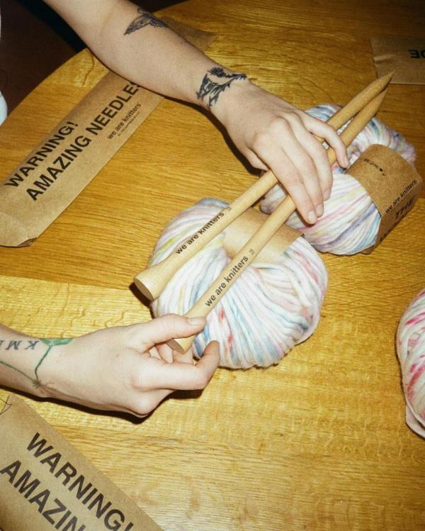 Photo from Ella Emhoff's Instagram shows hands gripping two knitting sticks that have the phrase 