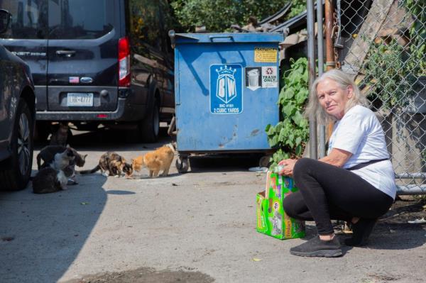 Regina Massaro sitting on the ground, feeding stray cats in the auto repair area of Willets Point, NY