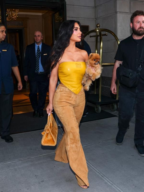 Kim Kardashian in a yellow outfit leaving The Ritz-Carlton in New York City on August 14, 2024, holding a small dog