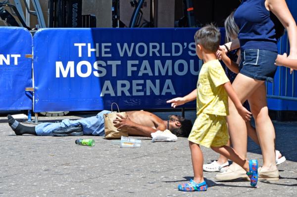 A child walking past a homeless man sleeping on the ground outside of Penn Station on Aug. 27, 2024.