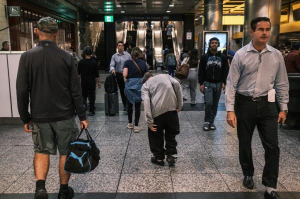 Commuters walking past a homeless man standing by the escalators in Penn Station on Aug. 22, 2024.