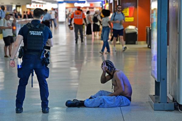 A shirtless person sitting on the floor of Penn Station.