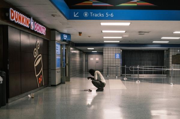 A man squatting outside of the Dunkin' Do<em></em>nuts in the station.