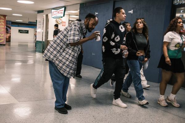 A group of people walking past a homeless man who appears to be panhandling in Penn Station.