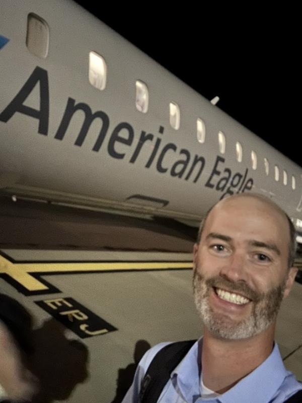 Photo of a smiling man in front of an airplane. 