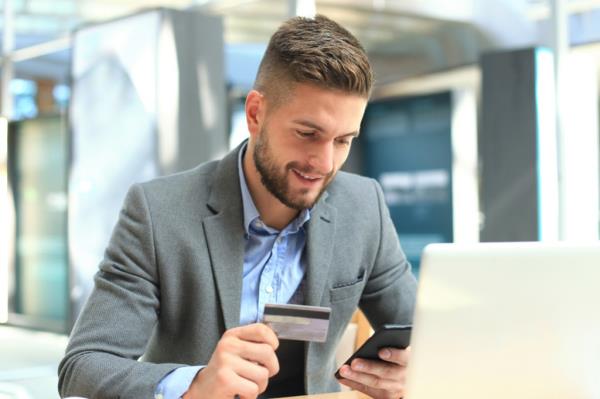 Happy young businessman using laptop and credit card at the table.