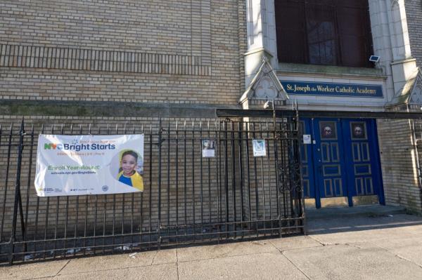 Side entrance of St. Joseph the Worker Catholic Academy with sign advertising pre-K and 3-k hanging on fence.