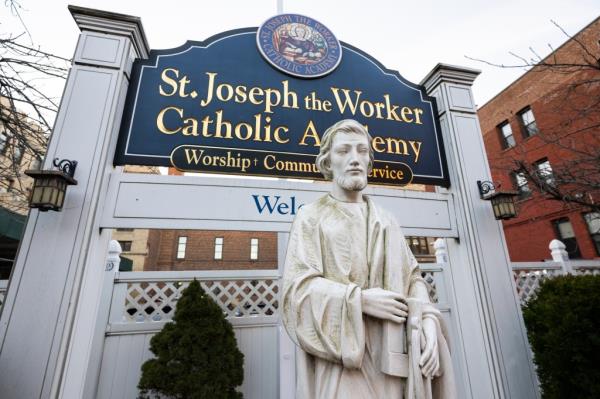 Statue of Joseph The Worker outside SJW Catholic Academy next to sign with school name and address in Brooklyn, NY.