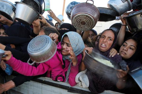 Palestinians gather with pots at a charity kitchen to receive food.