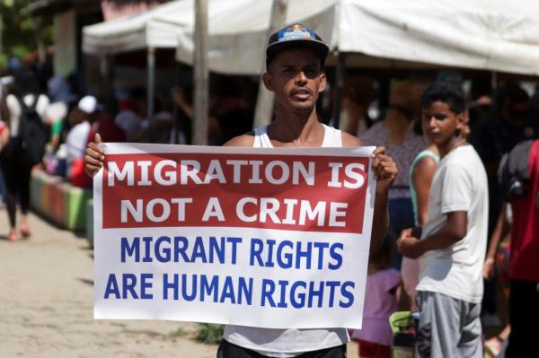 A pro migrant protestor holding sign that says Migration is not a crime 