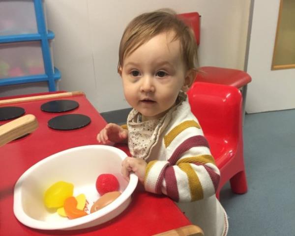 Baby Maggie-Mae sat on red plastic chair, playing with toys