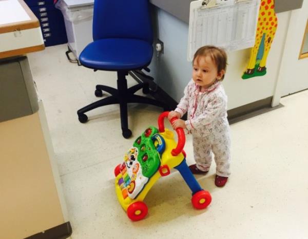 Baby Maggie-Mae in hospital, standing upright playing with toy