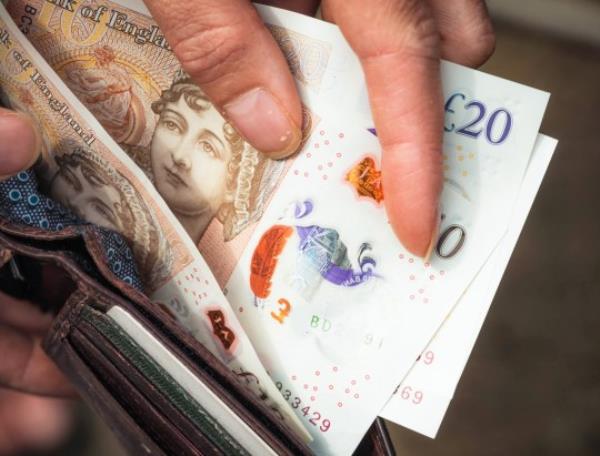 Close-up up as ten and twenty pound notes are taken out of a wallet for payment.