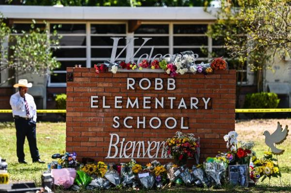 Sign for Robb Elementary School surrounded by flowers in a vigil.