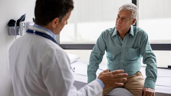 Man in blue shirt talks to physician.