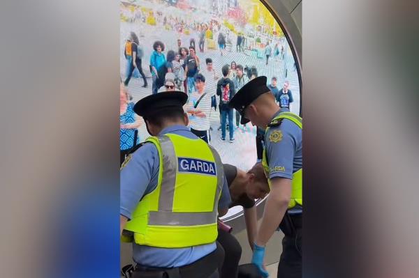 Police in Dublin arresting a woman bending over in front of the video screen.