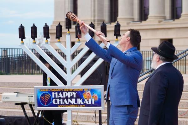 Gov. Kevin Stitt lights a candle on a large menorah.