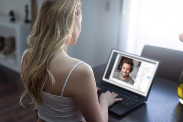 Young blo<em></em>nde woman sitting at a desk using a laptop for an o<em></em>nline date with a handsome man