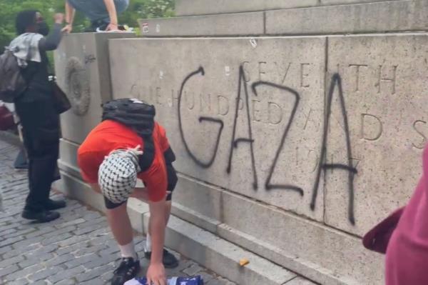 Protesters burning US flag at the ba<em></em>se of the 107th Infantry Memorial, climbing the statue, waving Palestinian flags and marking it with 'GAZA' graffiti and Palestinian flag stickers.