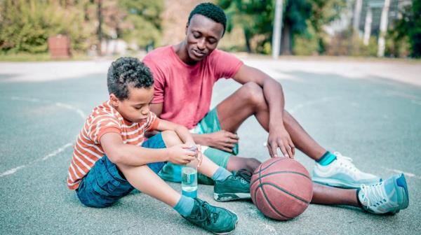 father and son sit and talk on basketball court