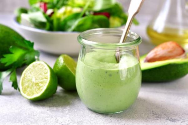 Homemade avocado yogurt dressing in a vintage glass jar with ingredients for making on a light slate, stone or co<em></em>ncrete background.