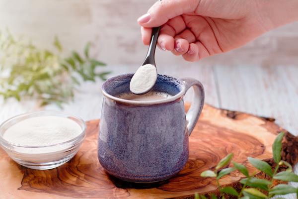 Hand adding collagen powder to a mug of coffee on a wooden board