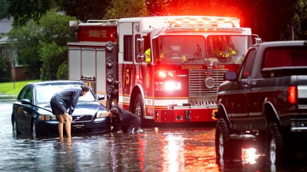 People attach a towline to a stranded vehicle on a flooded street after heavy rain from Tropical Storm Debby, Monday, Aug. 5, 2024, in Savannah, Ga. (AP Photo/Stephen B. Morton)