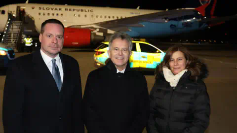 Department of Health Two men and a woman standing on the tarmac at an airport in front of a place with the words 